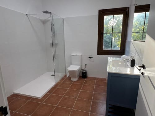 Salle de bain moderne à l'auberge rurale Can Ricós à Vallgorguina avec douche vitrée, toilettes, lavabo et vue sur la forêt
