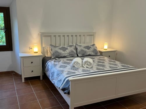 Chambre lumineuse à l'auberge rurale Can Ricós à Vallgorguina avec lit blanc, literie à motifs et éclairage chaleureux