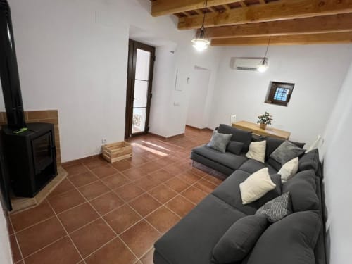 Spacieuse salle commune de l'auberge rurale Can Ricós à Vallgorguina avec canapé foncé, carrelage terre cuite, poutres en bois