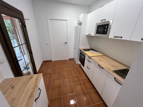 Cuisine moderne de l'auberge rurale Can Ricós à Vallgorguina avec armoires blanches, comptoirs en bois et carrelage en terre cuite