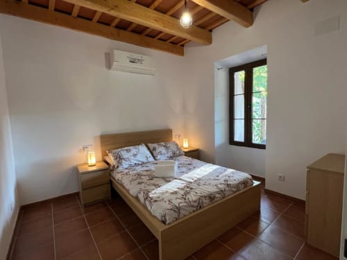 Chambre rustique à l'auberge rurale Can Ricós à Vallgorguina avec poutres en bois, sol en terre cuite et vue sur le jardin