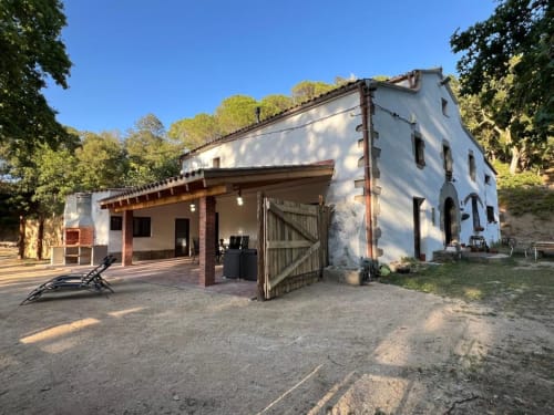 Gîte rural Can Ricós à Vallgorguina, Barcelone - bâtiment blanc avec terrasse en bois et patio entourés
