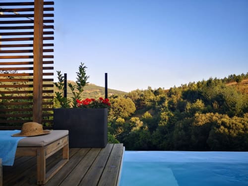 Terraço com piscina infinita em Em Xisto: flores vermelhas, espreguiçadeira de madeira e vista para montanhas florestadas em Góis, Portugal