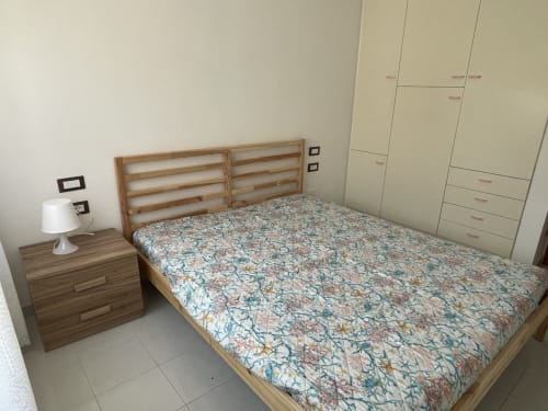 Accogliente camera da letto presso Rigiariloo Home Apartments con letto in legno, biancheria a motivi, comodino, lampada e armadio a muro