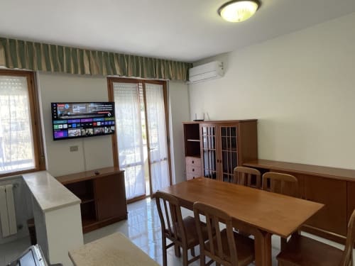 Soggiorno moderno con tavolo da pranzo, TV, arredamenti in legno e vista mare presso Rigiariloo Home Apartments in Italia