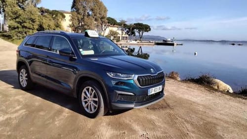 Blue Skoda SUV taxi parked on beach near Alma Rossa hotel in Lecci, Corsica, with calm bay and boats