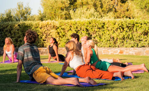 Group yoga class on grass at Villa Freedom in Crete with lush green hedges backdrop
