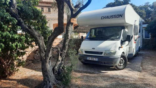 Camping-car Chausson garé dans l'espace ombragé du Camping La Lézardière à La Valette du Var, avec arbres et bâtiment en pierre