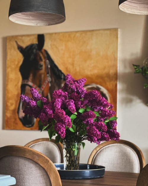 Fleurs de lilas violettes dans un vase sur la table à manger de La Maison De Fleurat, avec un portrait équestre et des luminaires suspendus