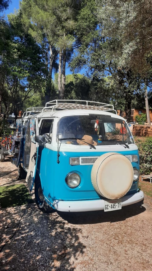 Vintage Combi VW bleu et blanc au Camping La Lézardière, entouré de grands arbres et d'un jardin