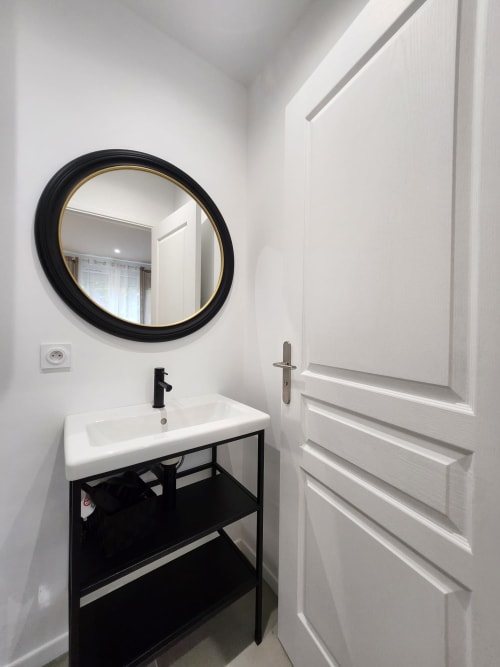 Salle de bain moderne à l'Appart Hôtel Panambi avec miroir rond noir, lavabo blanc, meuble vasque noir et porte blanche