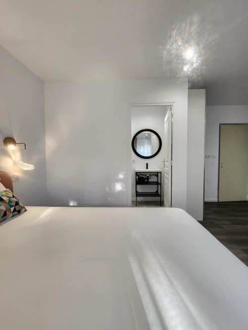 Chambre moderne à l'Appart Hôtel Panambi avec lit blanc, miroir circulaire et coiffeuse noire à Chevilly-Larue