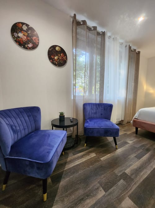 Chambre moderne à l'Appart Hôtel Panambi avec fauteuils velours bleu, table d'appoint et rideaux voilages donnant sur Chevilly-Larue