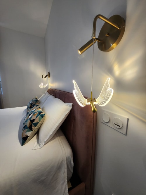 Chambre moderne de l'Appart Hôtel Panambi avec applique murale dorée, néons ailes et tête de lit bordeaux