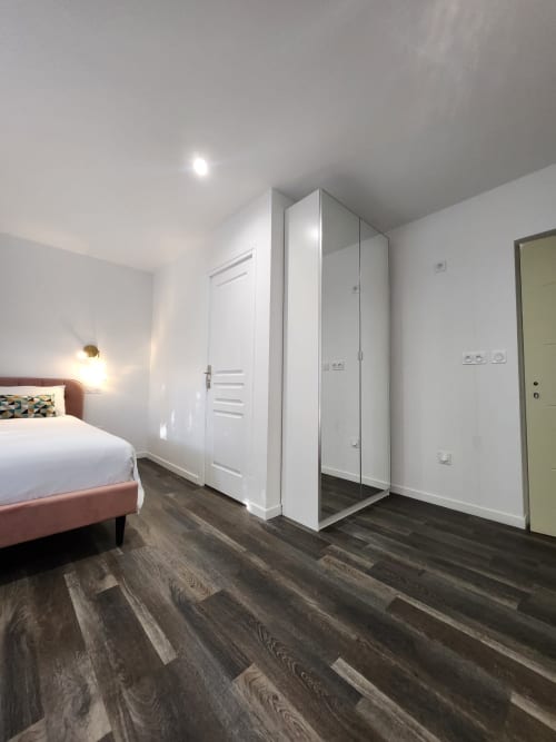 Chambre moderne à l'Appart Hôtel Panambi avec lit, douche vitrée et parquet en bois foncé