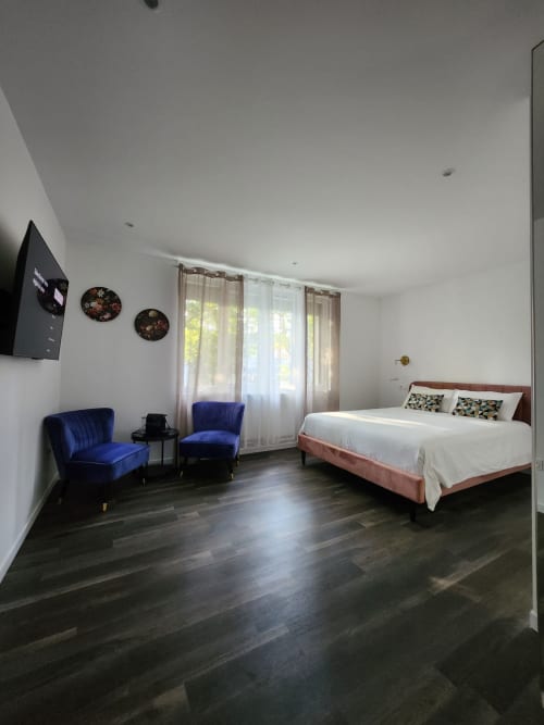 Chambre moderne à l'Appart Hôtel Panambi avec fauteuils en velours bleu, lit queen-size, parquets foncés et vue sur la ville