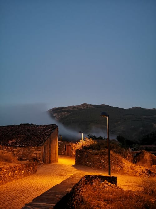 Refúgio de montanha Em Xisto em Góis ao entardecer com edifícios de pedra, candeeiro e encosta enevoada