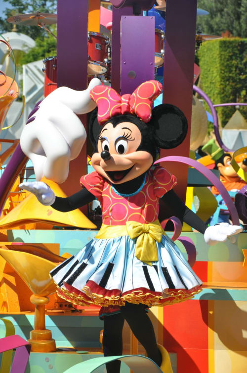 Minnie Mouse character waving at colorful theme park parade float near Isigny-sur-Mer