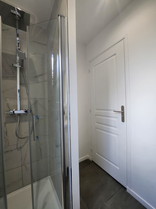 Salle de bain moderne à l'Appart Hôtel Panambi avec douche vitrée, carrelage marbre et porte blanche