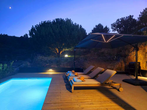 Piscina iluminada da villa de montanha Em Xisto em Góis, Portugal, com espreguiçadeiras e sombrinha ao entardecer