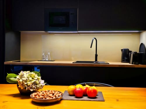 Cozinha moderna com torneira preta, painel traseiro amarelo e área de refeições com frutas e flores frescas na vila Em Xisto, Góis
