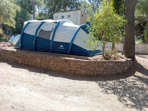 Tente tunnel bleu et blanc au Camping La Lézardière à La Valette du Var, entourée d'arbres et de murs en pierre