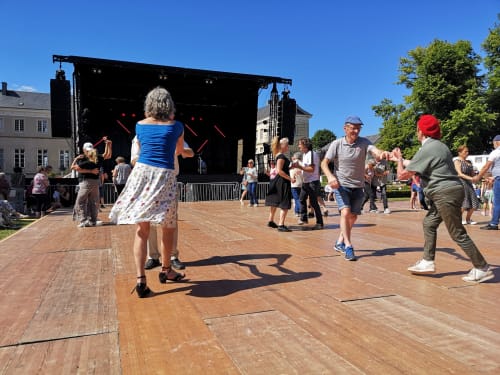 Outdoor street festival with people dancing near stage in Isigny-sur-Mer square on sunny day