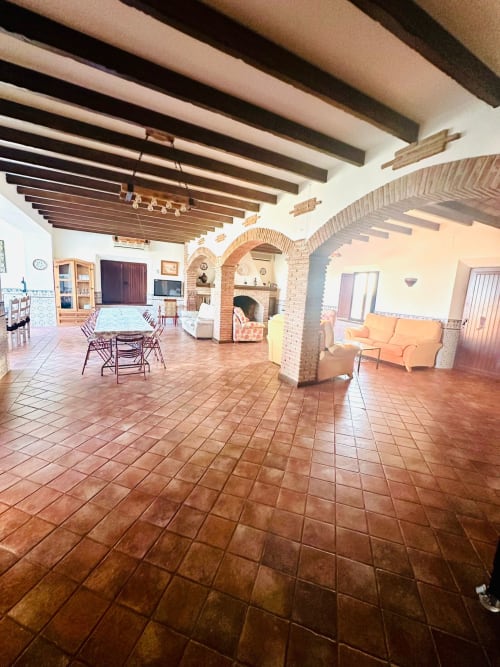 Amplia sala de estar en cabaña de Mérida con pisos de barro, vigas de madera, arcos de ladrillo y vistas a las montañas