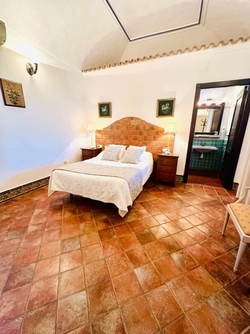 Amplia habitación de cabaña en Mérida con piso de barro, cabecero de ladrillo y vistas a las montañas