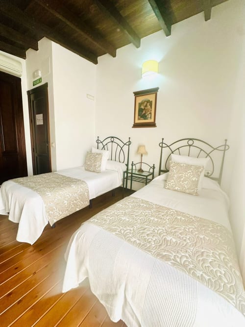 Dormitorio de cabaña en Mérida con tres camas individuales, cabeceros de hierro ornamentales, ropa blanca, vigas de madera y vista a la montaña