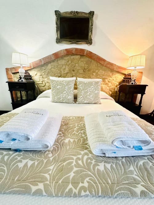 Dormitorio de lujo en Mérida con cabecero ornamentado, toallas blancas y almohadas decorativas