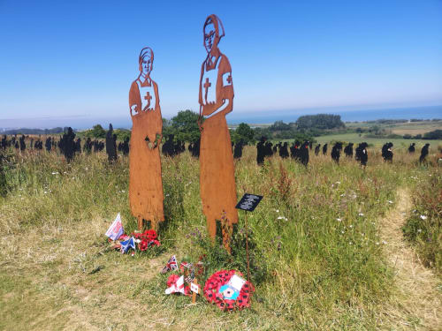 Memorial statues with red flowers in Normandy field near Isigny-sur-Mer, France