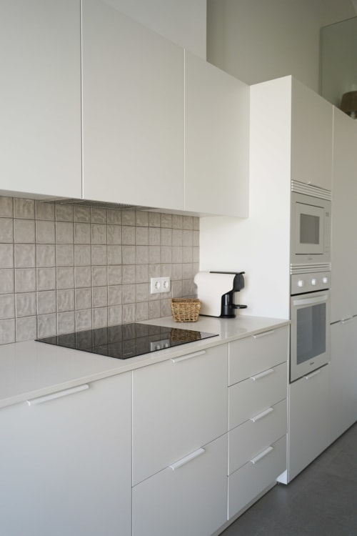 Cozinha moderna da villa Casa Barranco em Bordeira com armários brancos, azulejos cinzentos e placa de indução preta