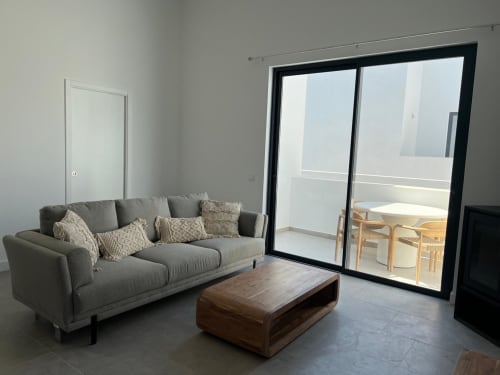 Sala de estar moderna com sofá cinzento, mesa de madeira e vista para o mar pela porta de vidro na villa Casa Bordeira em Bordeira,