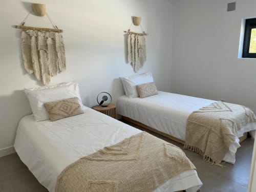 Quarto duplo da villa Casa Bordeira em Bordeira com camas brancas, têxteis bege, macramés na parede e vista para o mar.