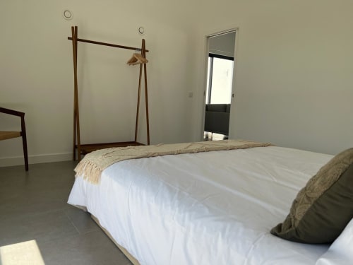 Quarto minimalista com cama com dossel de madeira, roupa de cama branca e vista para o mar na quinta Casa Bordeira em Bordeira, Portugal