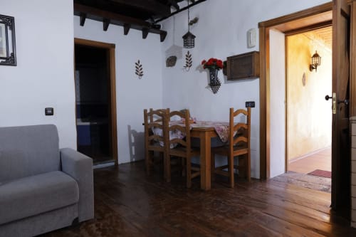 Rustic cottage interior in Icod de los Vinos with wooden dining table, gray sofa, and white walls with decorative accents.
