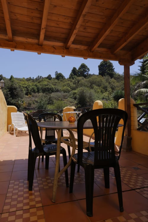Shaded terrace with dining table and black chairs overlooking green hillside at Casonas de Marengo cottage in Icod de los
