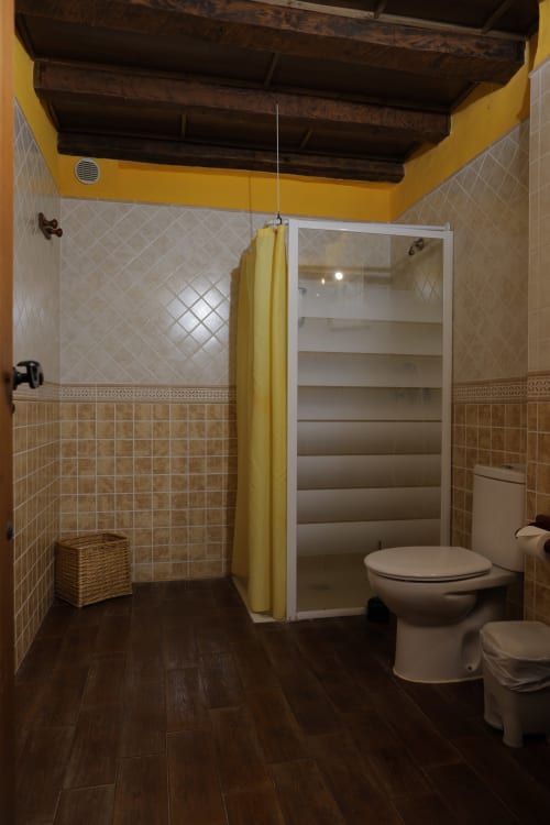 Modern bathroom with yellow ceiling, white tile walls, dark wood floor, glass shower enclosure, and toilet at Casonas de