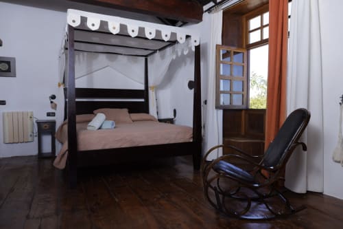 Elegant bedroom with black four-poster bed, white sheer curtains, dark wood floors, and wooden door opening to garden at