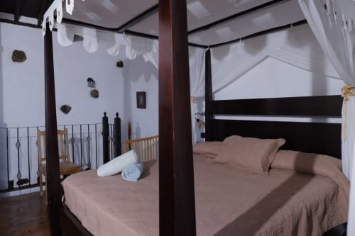 Spacious bedroom with black four-poster bed, beige bedding, white curtains, and white walls at Casonas de Marengo cottage in