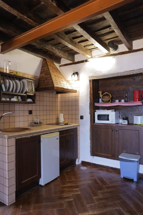 Rustic cottage kitchen at Casonas de Marengo with exposed beams, tile counters, dark wood cabinets, and modern appliances