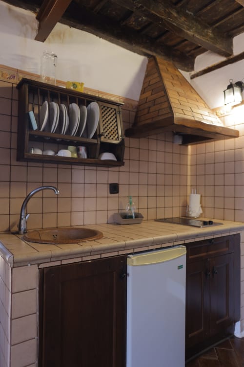 Rustic kitchen with dark wood cabinets, tiled countertop, round sink, plate rack, wooden hood, and exposed beams at Casonas
