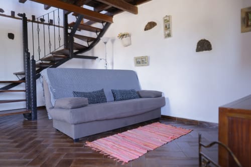 Cozy living room with grey futon sofa, wooden staircase, and pink rug at Casonas de Marengo cottage