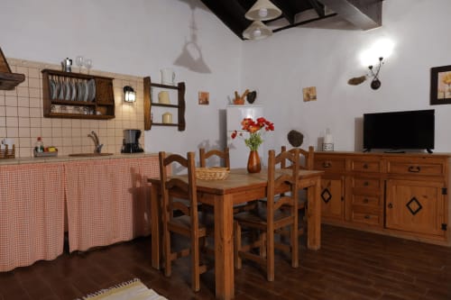 Rustic cottage kitchen and dining area with wooden furniture, red checkered accents, and mountain views at Casonas de