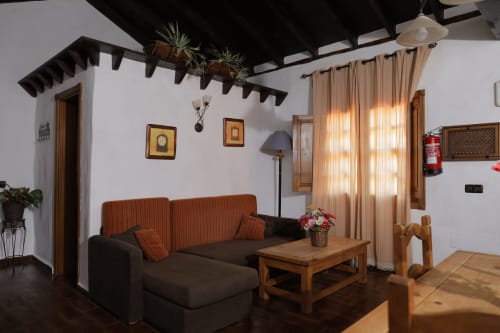 Rustic cottage living room at Casonas de Marengo with brown sofa, wooden beams, and mountain views through curtained windows