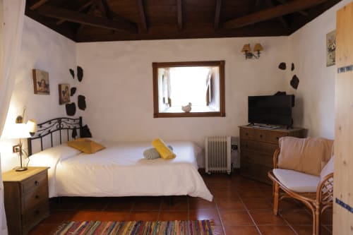 Rustic bedroom at Casonas de marengo in Icod de los Vinos with white bed, wooden beams, TV, and mountain views