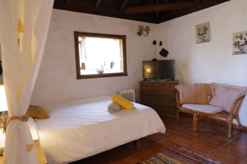 Bright bedroom in Casonas de Marengo cottage with canopy bed, rattan seating, TV, mountain views through window, terracotta