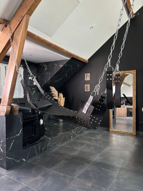 Suite luxe moderne aux Doucesunits45 à Montargis : murs en marbre noir, poutres bois et fauteuil suspendu élégant