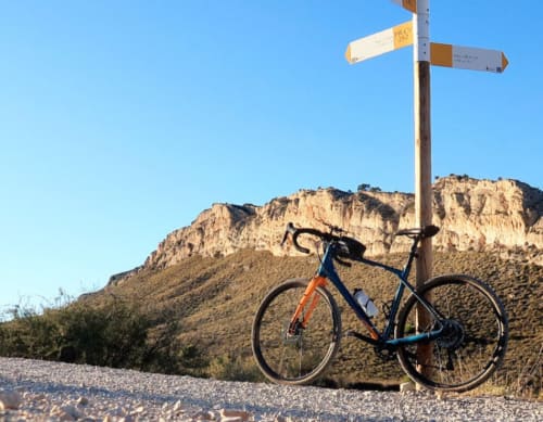 Bicicletta blu appoggiata a un palo segnaletico con le montagne desertiche di Vallgorguina, Barcellona, sullo sfondo